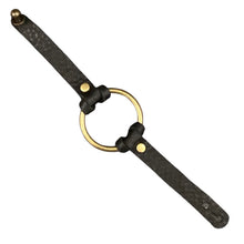 A black leather strap accessory with a large central brass ring, two brass rivets, and a brass end cap, shown on a plain white background.